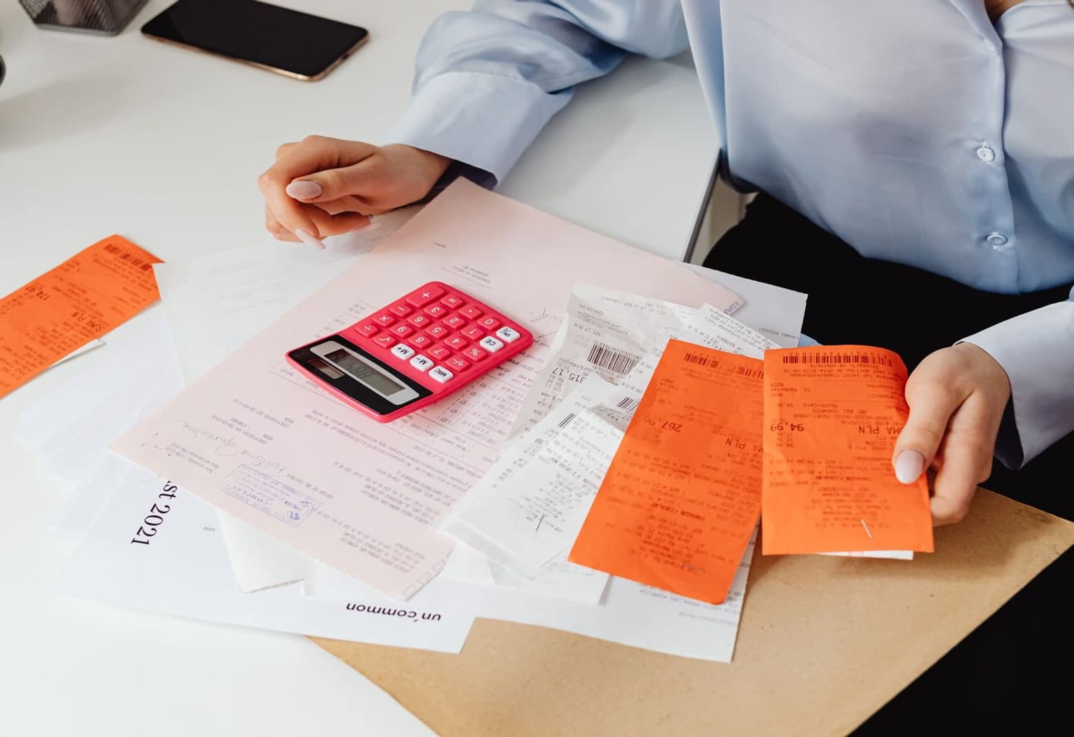 Logistics documents, receipts and a calculator spread across a desk while a person reviews them