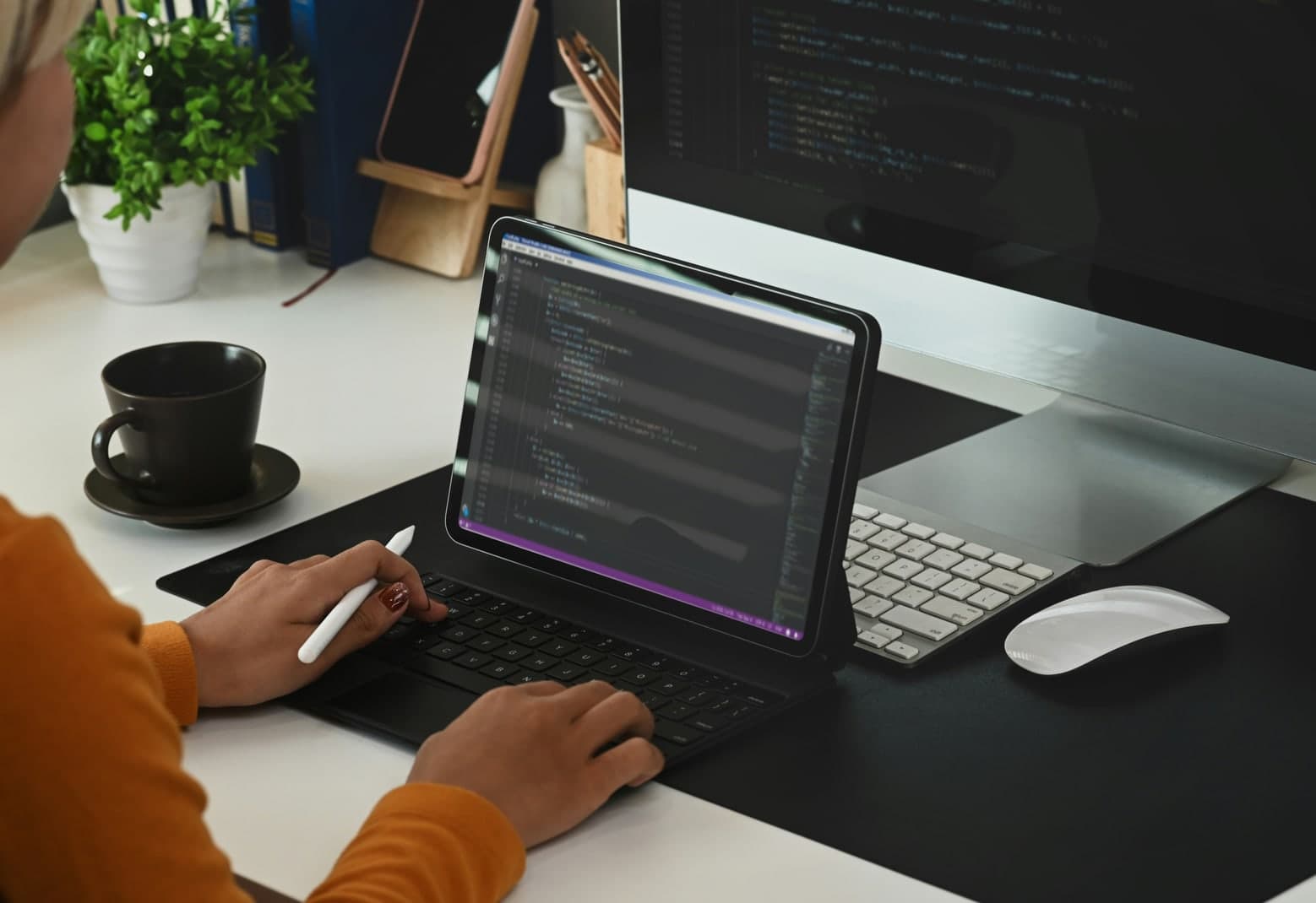 A person working on a tablet showing code at a desk with a coffee cup and plants